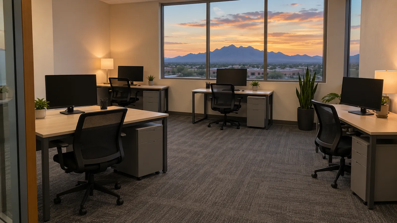 Small office with clean desks, dark screens and freshly vacuumed carpet at dusk